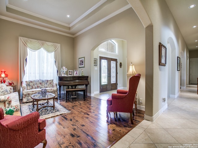 living area with arched walkways, a raised ceiling, french doors, and wood finished floors