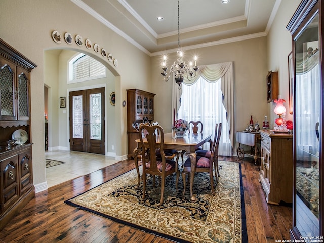 dining space featuring hardwood / wood-style floors, french doors, an inviting chandelier, arched walkways, and a raised ceiling