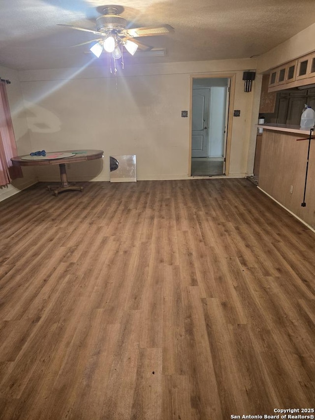 unfurnished living room with dark wood-type flooring, ceiling fan, a textured ceiling, and baseboards