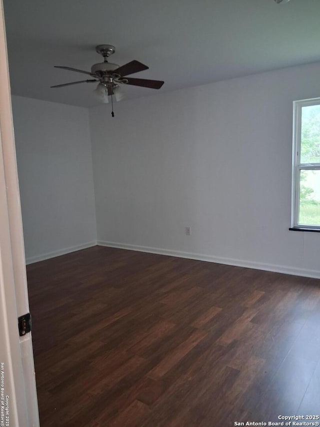 spare room with baseboards, dark wood-style floors, and a ceiling fan