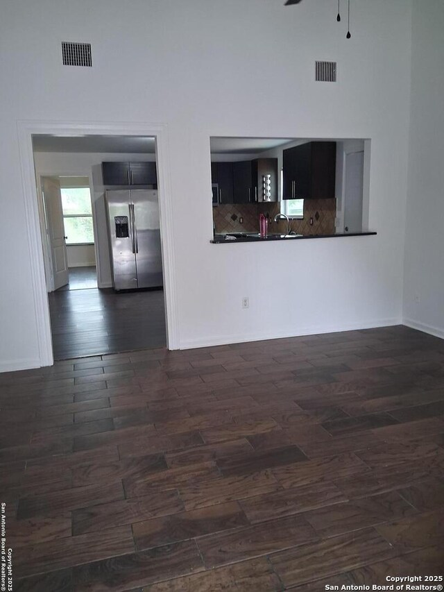 unfurnished living room with a sink, baseboards, dark wood-type flooring, and visible vents