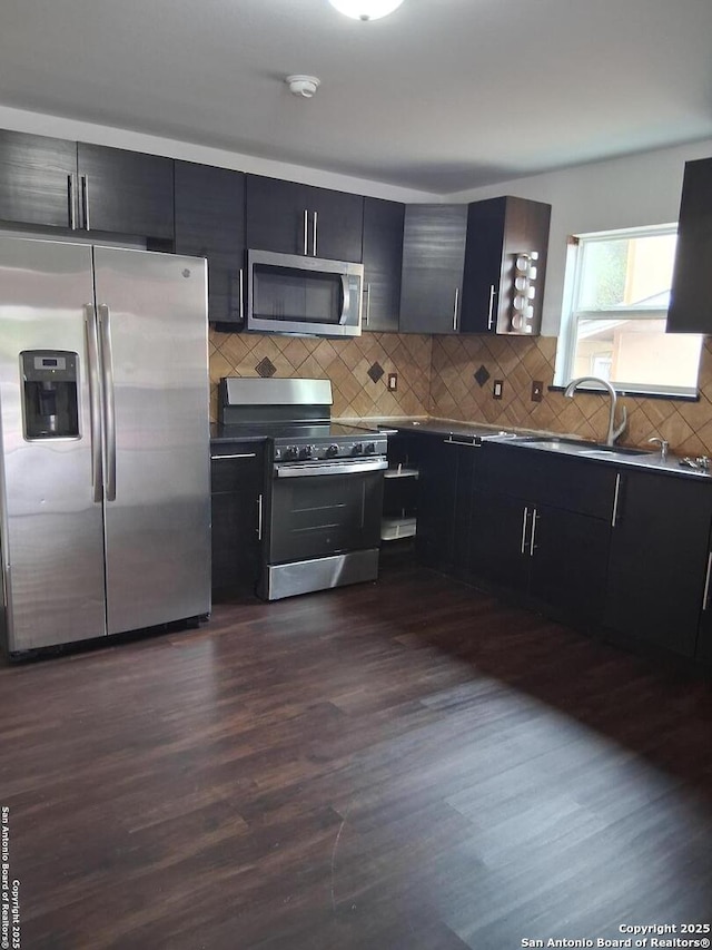 kitchen featuring a sink, tasteful backsplash, dark wood-type flooring, dark cabinets, and appliances with stainless steel finishes