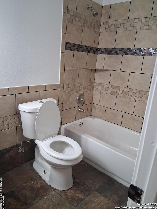 full bath with toilet, tile walls, shower / bathtub combination, and stone finish flooring