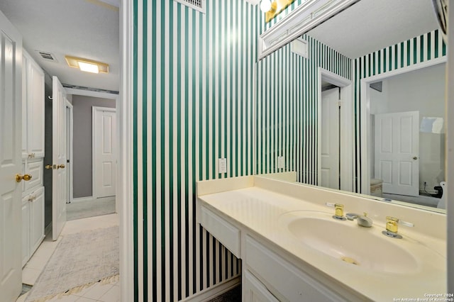 bathroom with wallpapered walls, visible vents, tile patterned flooring, baseboards, and vanity