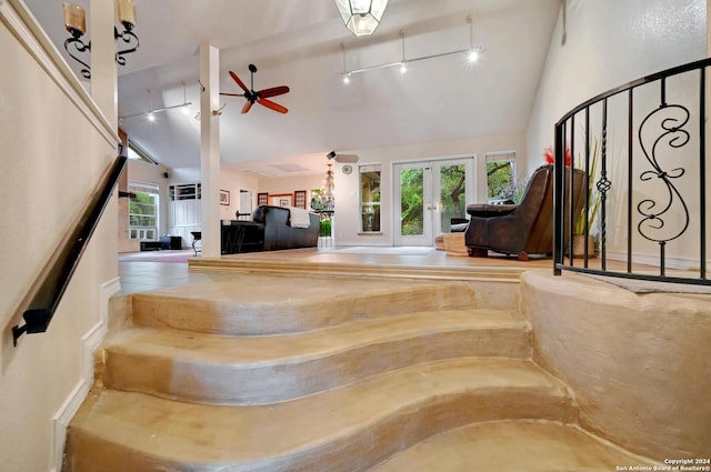 staircase with rail lighting, french doors, a ceiling fan, and high vaulted ceiling