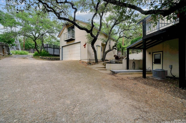 view of side of home with a balcony, driveway, a garage, stucco siding, and central AC unit