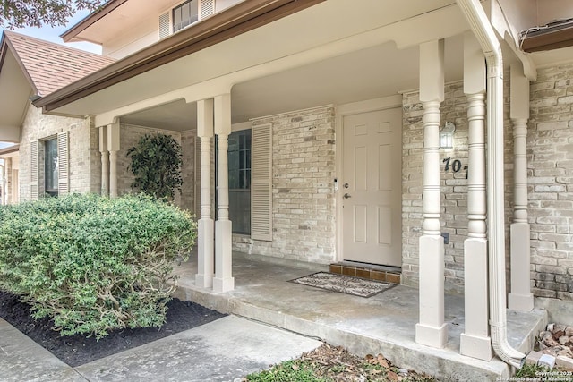 property entrance featuring a porch, brick siding, and a shingled roof