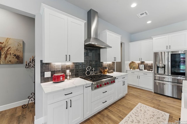 821 Bingham Ln, New Braunfels, TX 78132 - kitchen with stainless steel appliances, wall chimney range hood, light wood-style flooring, white cabinets, and light stone countertops