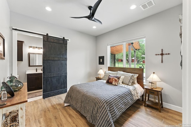 821 Bingham Ln, New Braunfels, TX 78132 - bedroom with ensuite bathroom, a barn door, light wood-type flooring, visible vents, and recessed lighting