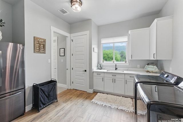 821 Bingham Ln, New Braunfels, TX 78132 - washroom featuring light wood finished floors, visible vents, a sink, separate washer and dryer, and cabinet space