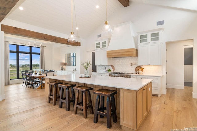 kitchen featuring a large island, beam ceiling, light wood-style flooring, and custom exhaust hood