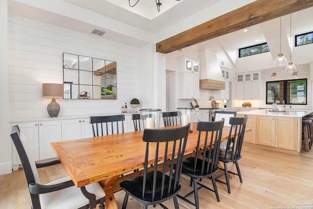 dining area with a towering ceiling, light wood-type flooring, visible vents, and beam ceiling