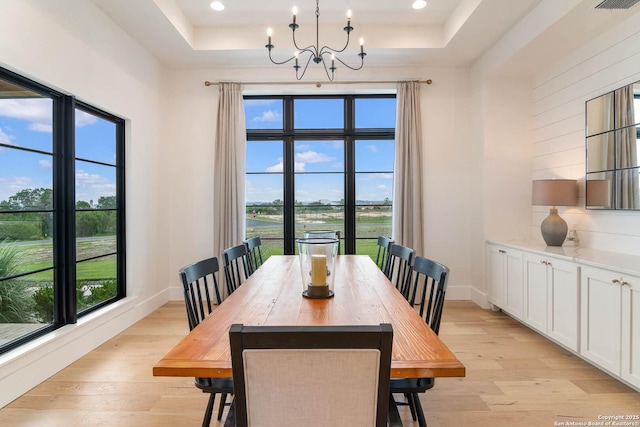 dining space with light wood finished floors, recessed lighting, a raised ceiling, and a notable chandelier