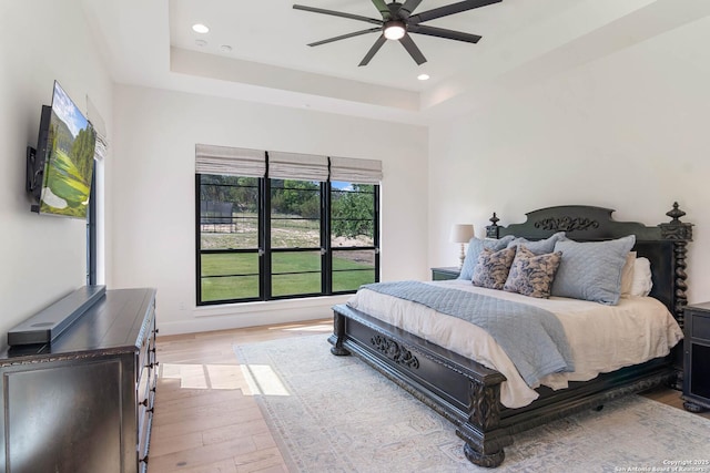 bedroom featuring a ceiling fan, light wood-style floors, a raised ceiling, and recessed lighting