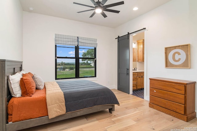 bedroom with a barn door, recessed lighting, light wood finished floors, connected bathroom, and baseboards