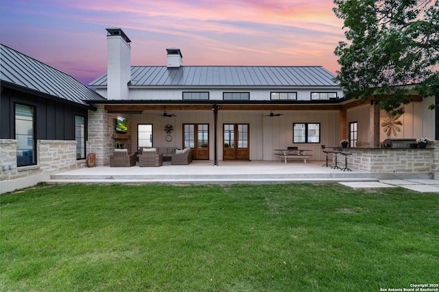rear view of property with a ceiling fan, a chimney, an outdoor living space, a yard, and a standing seam roof