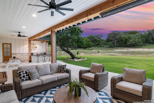 patio terrace at dusk featuring outdoor lounge area, a lawn, and ceiling fan