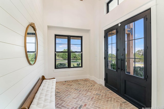 entrance foyer featuring french doors, wood walls, brick floor, and baseboards