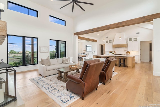 living area featuring light wood-type flooring, baseboards, ceiling fan, and high vaulted ceiling