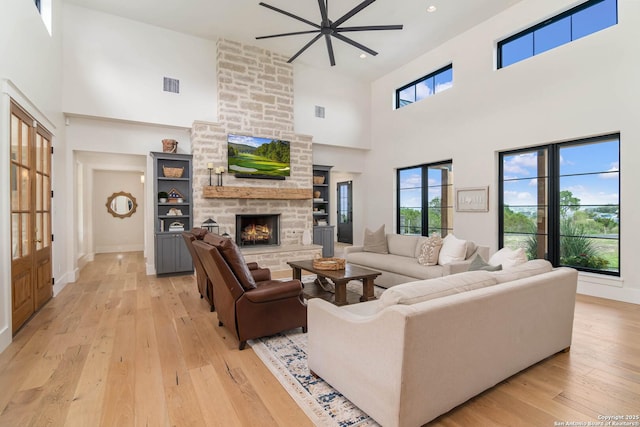 living room featuring a fireplace, a towering ceiling, light wood-type flooring, and visible vents