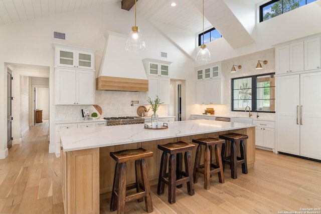 kitchen with high vaulted ceiling, visible vents, a kitchen island, tasteful backsplash, and custom exhaust hood