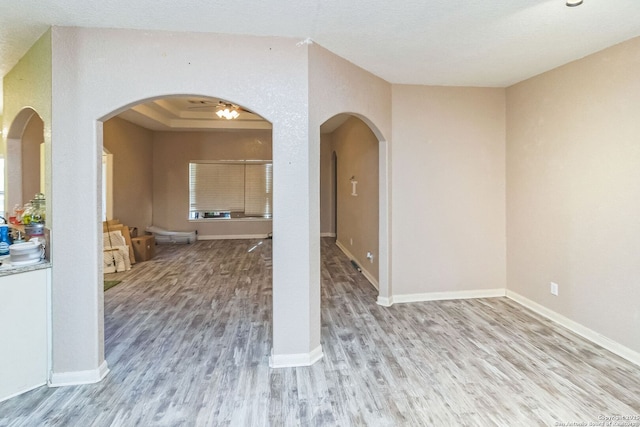 unfurnished room featuring arched walkways, baseboards, and wood finished floors
