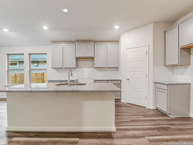 4532 Appaloosa Crst, San Antonio, TX 78245 - kitchen featuring a sink, light wood-type flooring, a kitchen island with sink, light stone counters, and recessed lighting