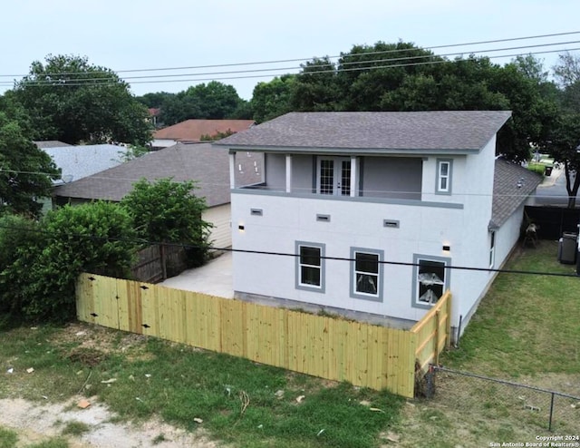 view of side of home with roof with shingles, french doors, a balcony, stucco siding, and a fenced backyard