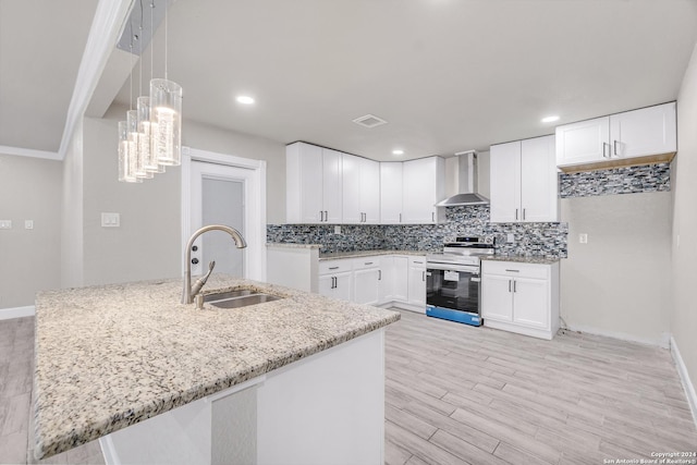 kitchen with a sink, wall chimney range hood, stainless steel range with electric stovetop, tasteful backsplash, and light stone counters