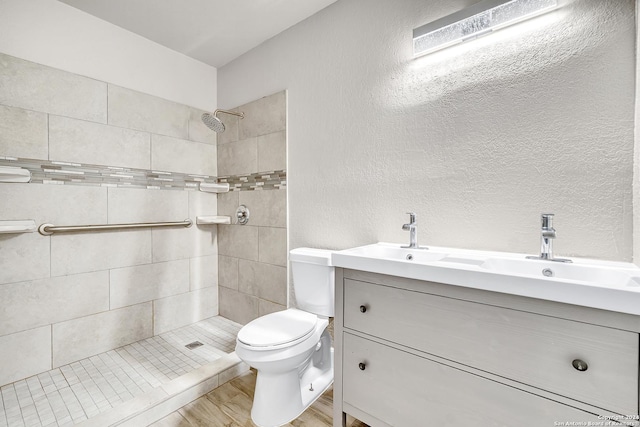full bath with vanity, toilet, a textured wall, and a tile shower