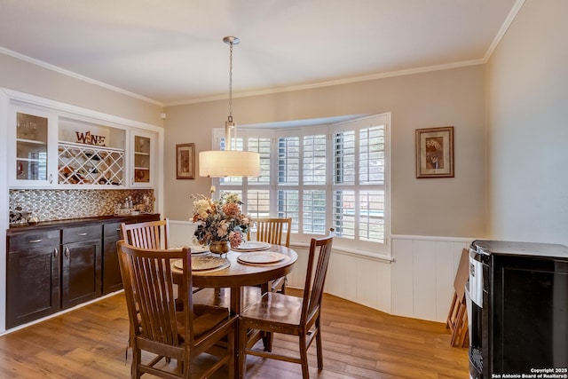 dining room featuring a bar, light wood-style floors, wainscoting, and ornamental molding