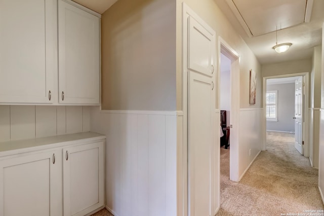 hallway featuring attic access, a wainscoted wall, and light colored carpet