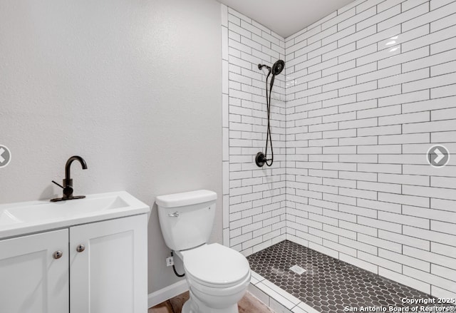 full bathroom featuring toilet, tiled shower, and vanity