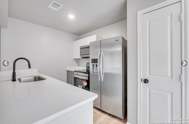 kitchen with a sink, light wood-style floors, visible vents, light countertops, and appliances with stainless steel finishes