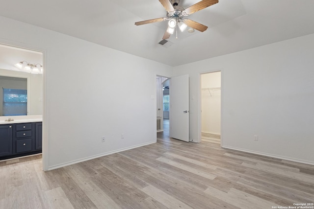 unfurnished bedroom with light wood-type flooring, a walk in closet, ensuite bathroom, and baseboards