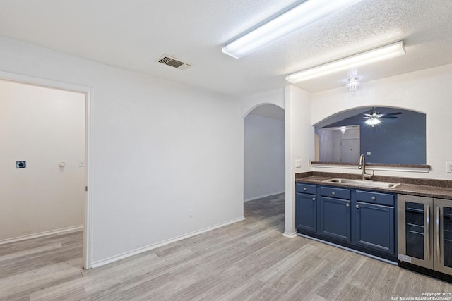 kitchen featuring a sink, wine cooler, blue cabinets, visible vents, and arched walkways