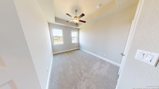 unfurnished room with carpet flooring, baseboards, a raised ceiling, ceiling fan, and a textured wall
