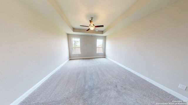 unfurnished room featuring a raised ceiling, carpet flooring, baseboards, and a ceiling fan