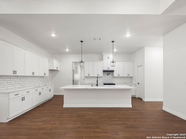kitchen with under cabinet range hood, tasteful backsplash, baseboards, and visible vents