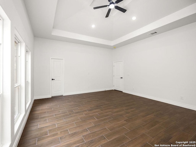 empty room with a tray ceiling, dark wood-style flooring, a ceiling fan, and visible vents