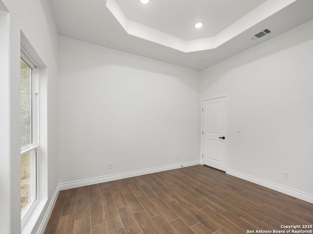spare room featuring a tray ceiling, dark wood-style flooring, baseboards, and visible vents