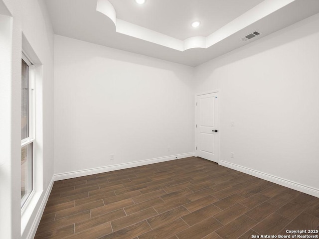 empty room with a tray ceiling, visible vents, baseboards, and dark wood-type flooring