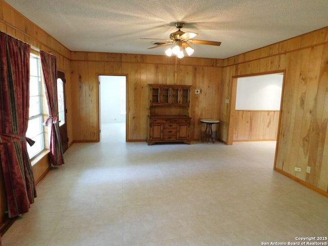 911 Austin, Sabinal, TX 78881 - unfurnished living room featuring a ceiling fan, light floors, wooden walls, and a healthy amount of sunlight