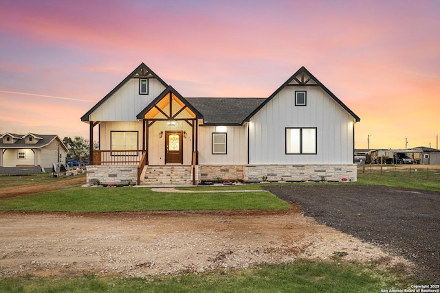 modern farmhouse featuring board and batten siding, a shingled roof, stone siding, and a lawn