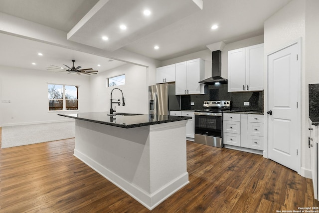 kitchen featuring a sink, a center island with sink, wall chimney range hood, appliances with stainless steel finishes, and decorative backsplash