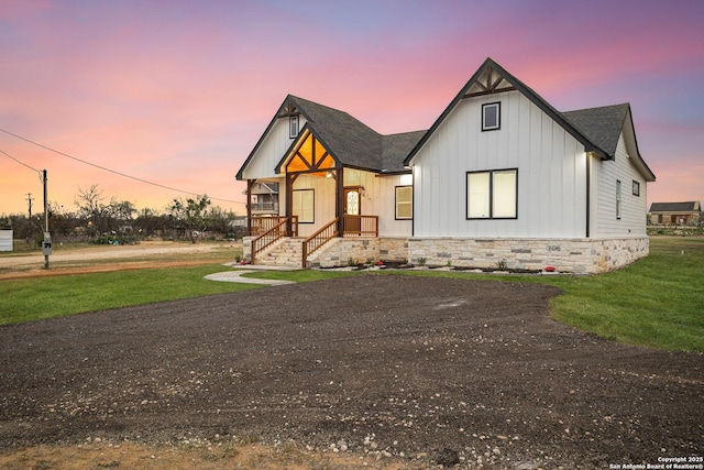 modern inspired farmhouse with stone siding, board and batten siding, a shingled roof, and a front lawn