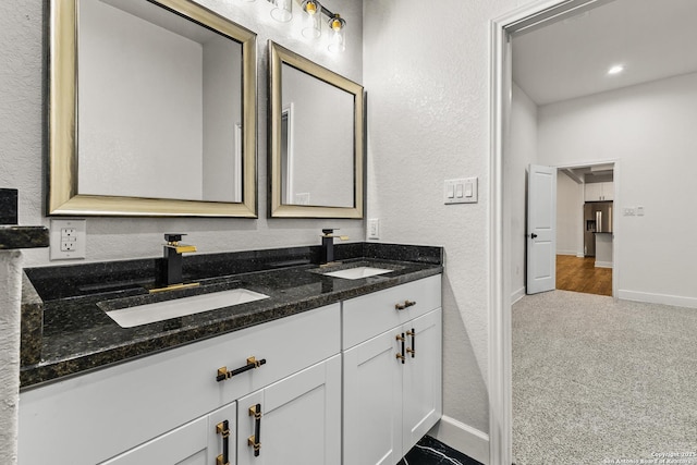 full bathroom with baseboards, double vanity, a sink, and a textured wall