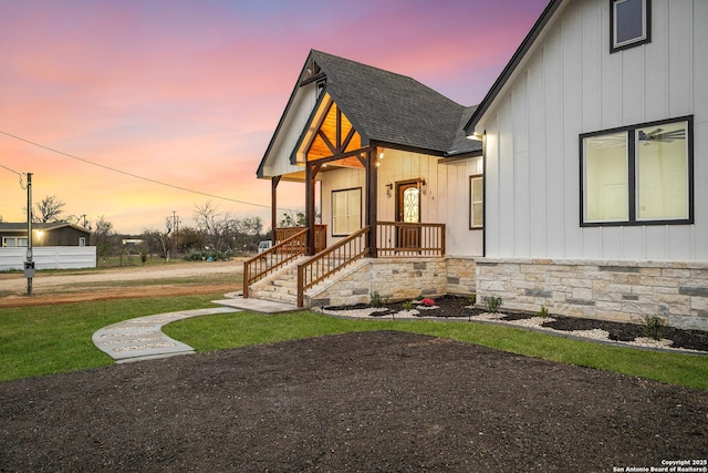 view of front of home with a yard, a shingled roof, and stone siding
