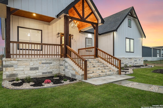 view of front of home with a front yard, roof with shingles, covered porch, and board and batten siding