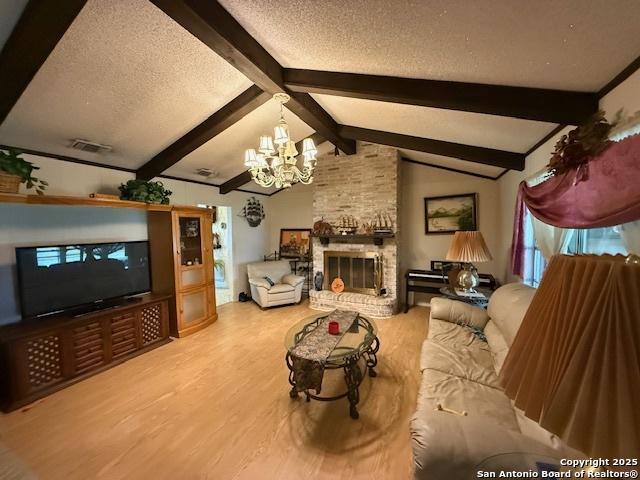 living area with an inviting chandelier, a textured ceiling, wood finished floors, and a brick fireplace
